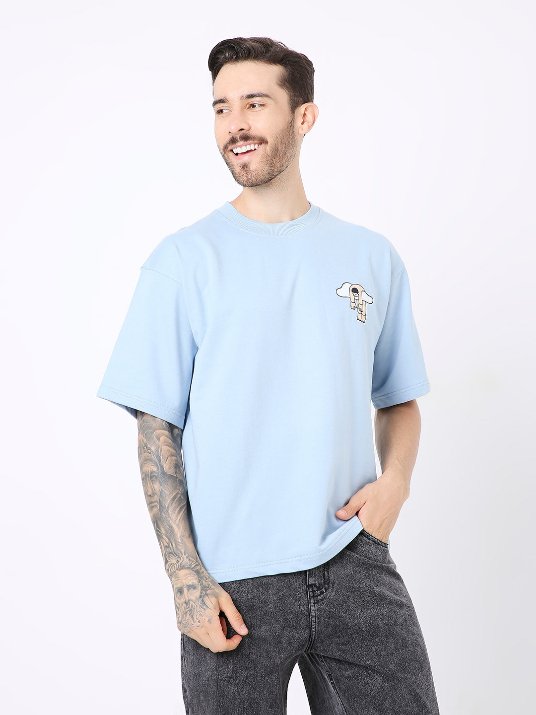 Light blue oversized t-shirt with small white and black graphic print on left chest, worn with black jeans.
