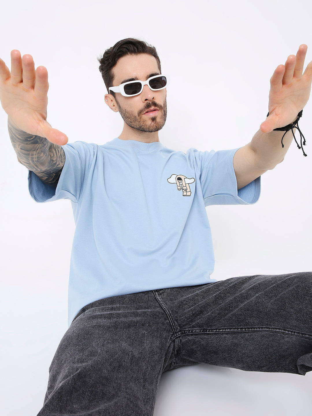 Light blue oversized T-shirt with small black and white graphic on chest, worn with black jeans and white sunglasses.