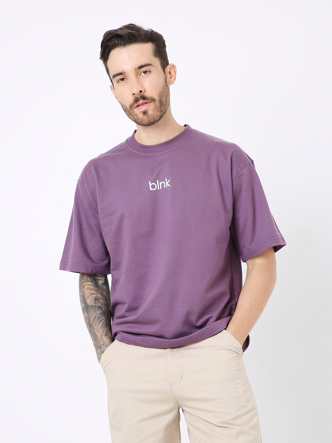Oversize purple t-shirt with small white "blink" text on front, short sleeves, worn with beige pants.