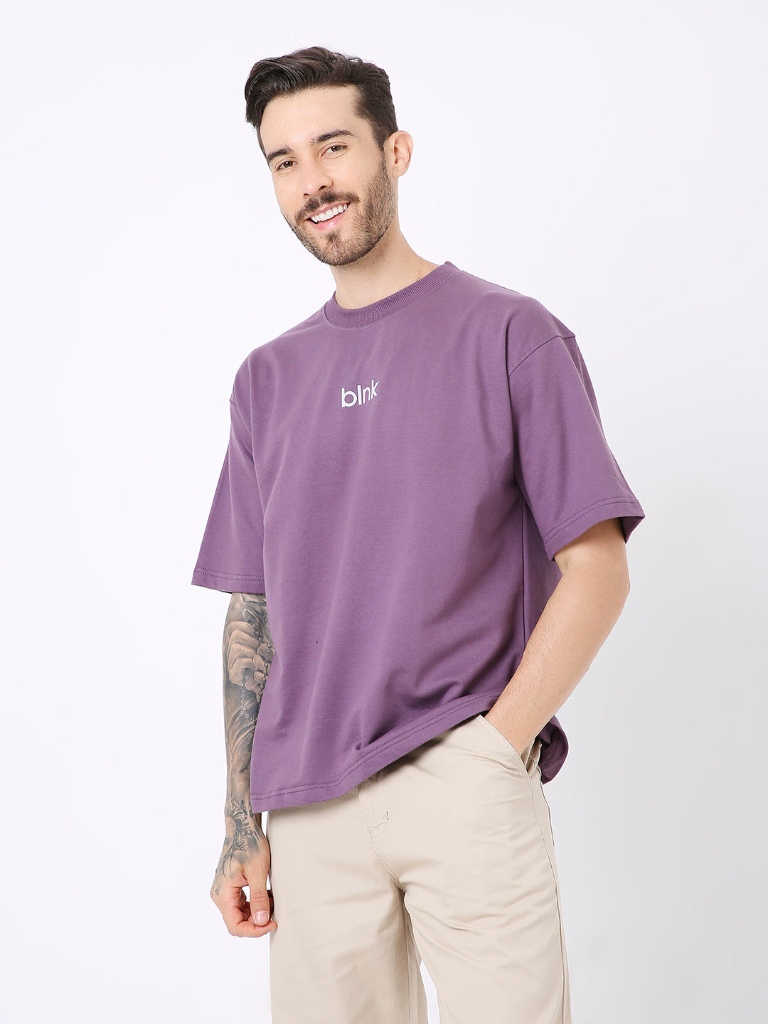 Oversize purple t-shirt with small white "dhv" logo on chest, worn with beige pants.