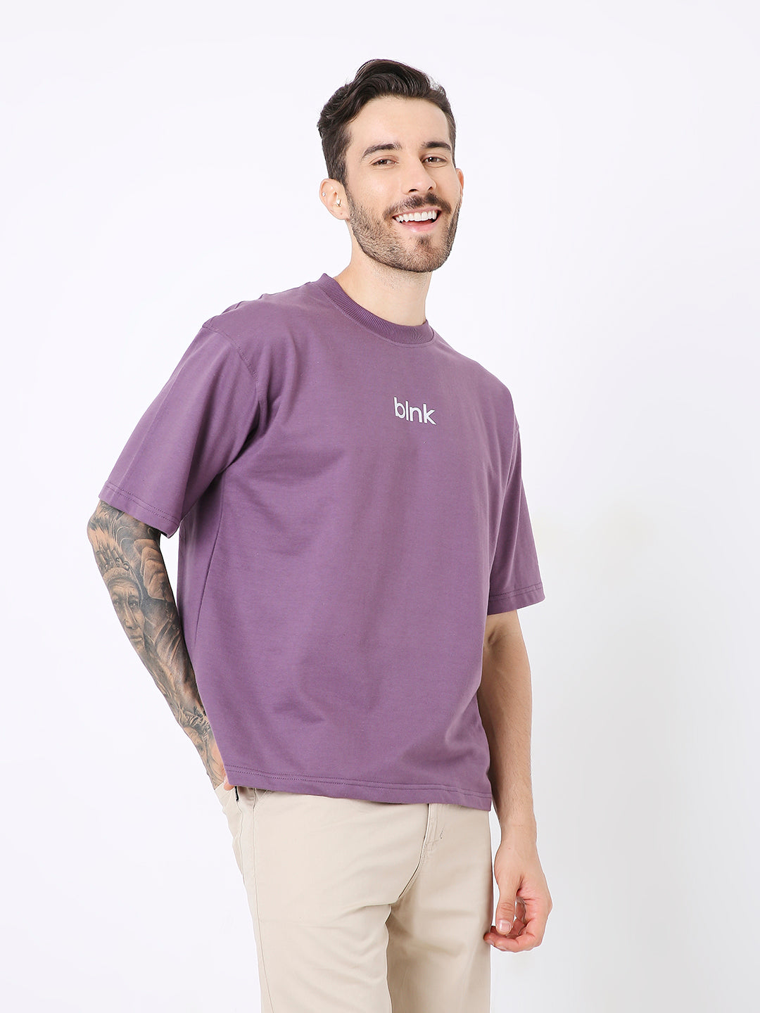 Oversize purple t-shirt with small white text on chest, worn with beige pants.