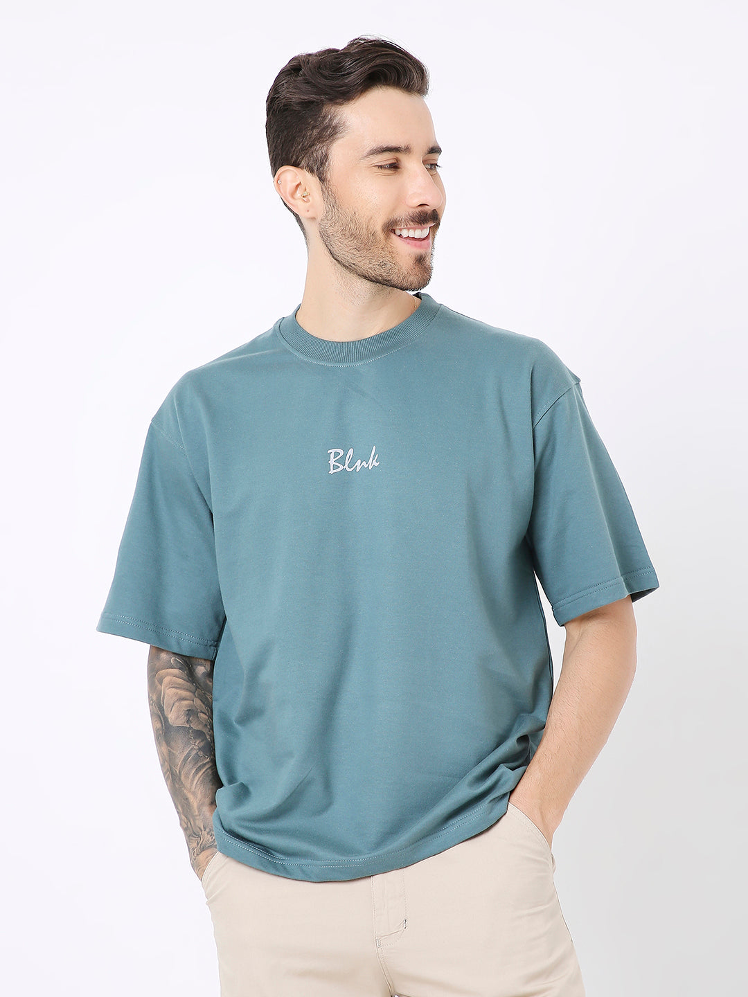 Oversize sapphire blue t-shirt with small white script logo on chest, worn with beige pants.