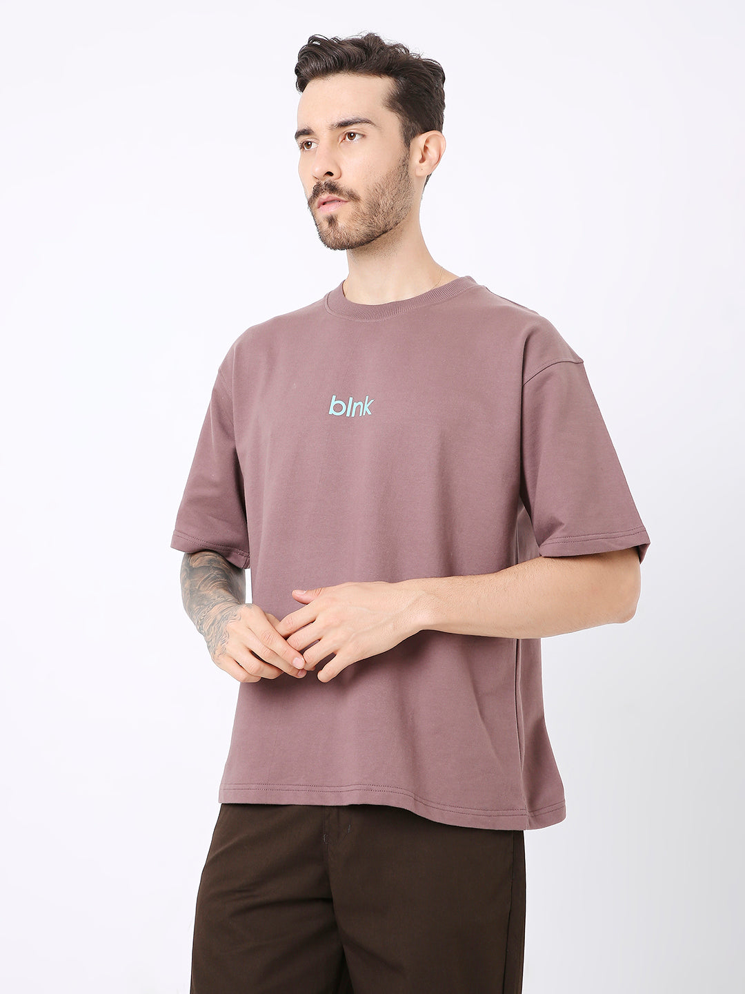 Oversized old rose t-shirt with small blue embroidered text on chest, worn with brown pants.