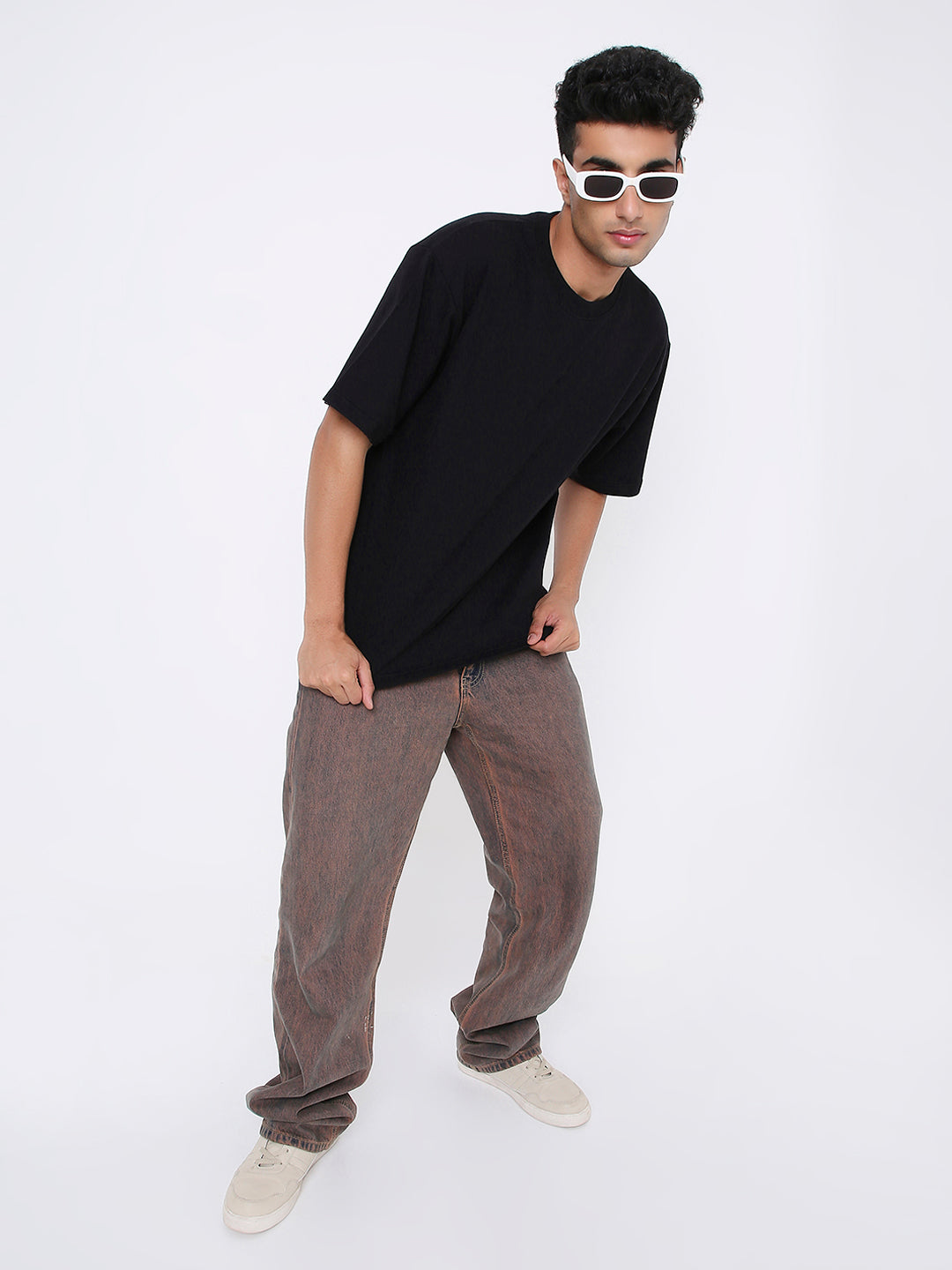 Oversize black solid short-sleeve t-shirt worn with brown pants and white sneakers.