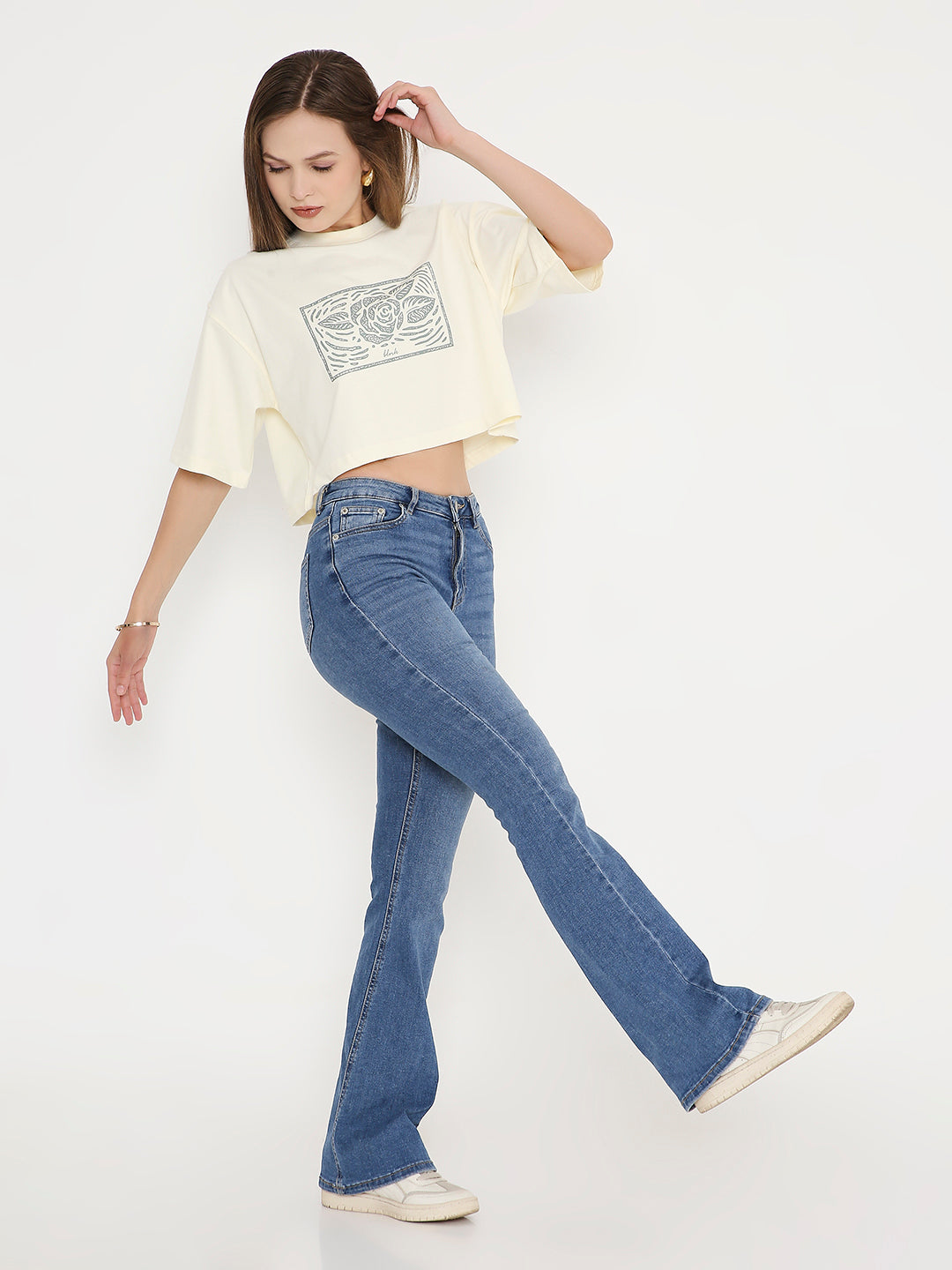 Off-white oversized crop top with black abstract print, short sleeves, paired with blue flared jeans.