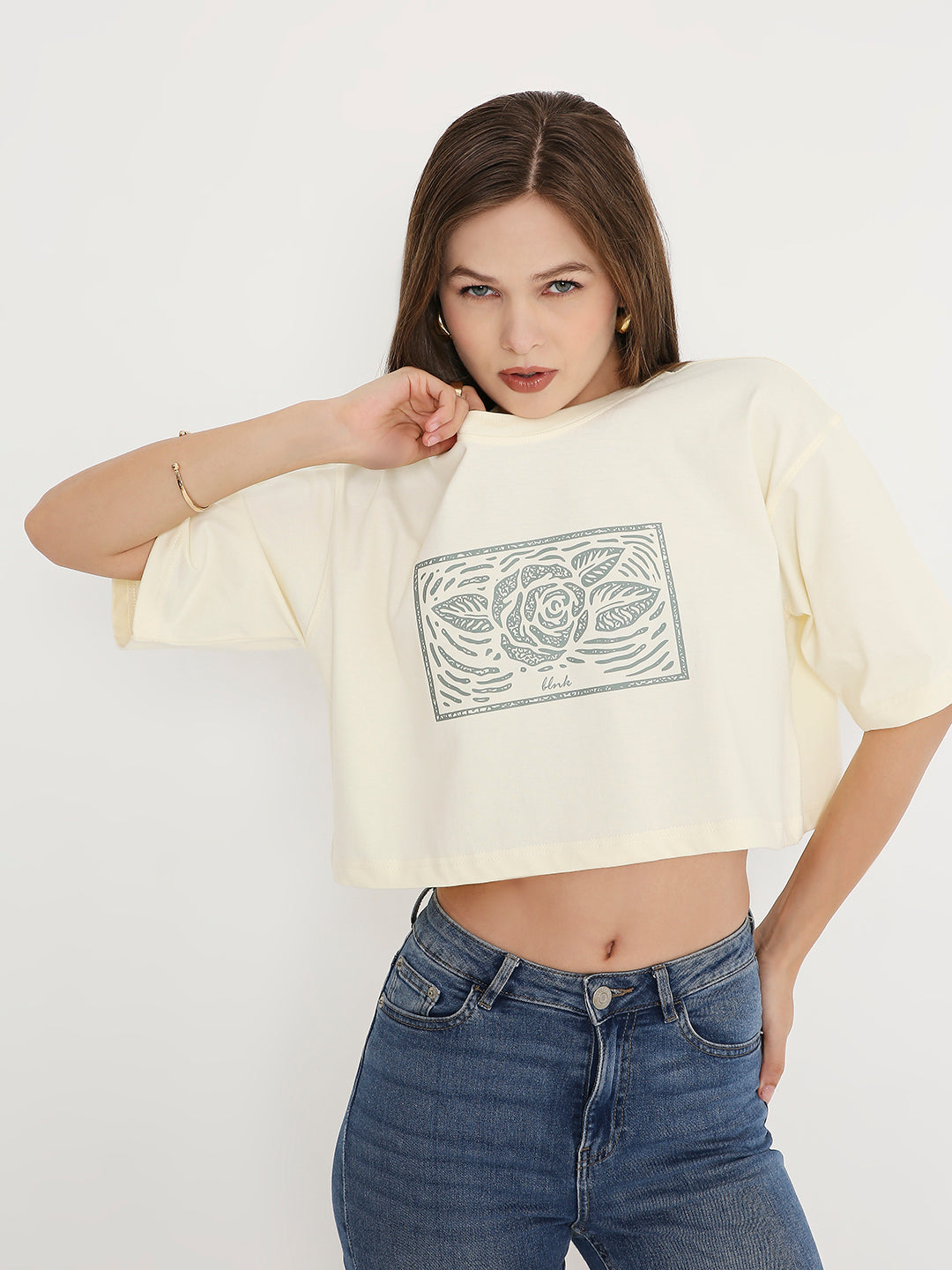 Off-white oversized crop top with black graphic print and dropped shoulders worn with blue jeans.