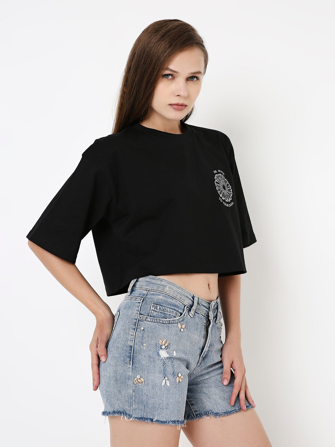 Oversize black crop top with white printed emblem on chest, paired with distressed light blue denim shorts.