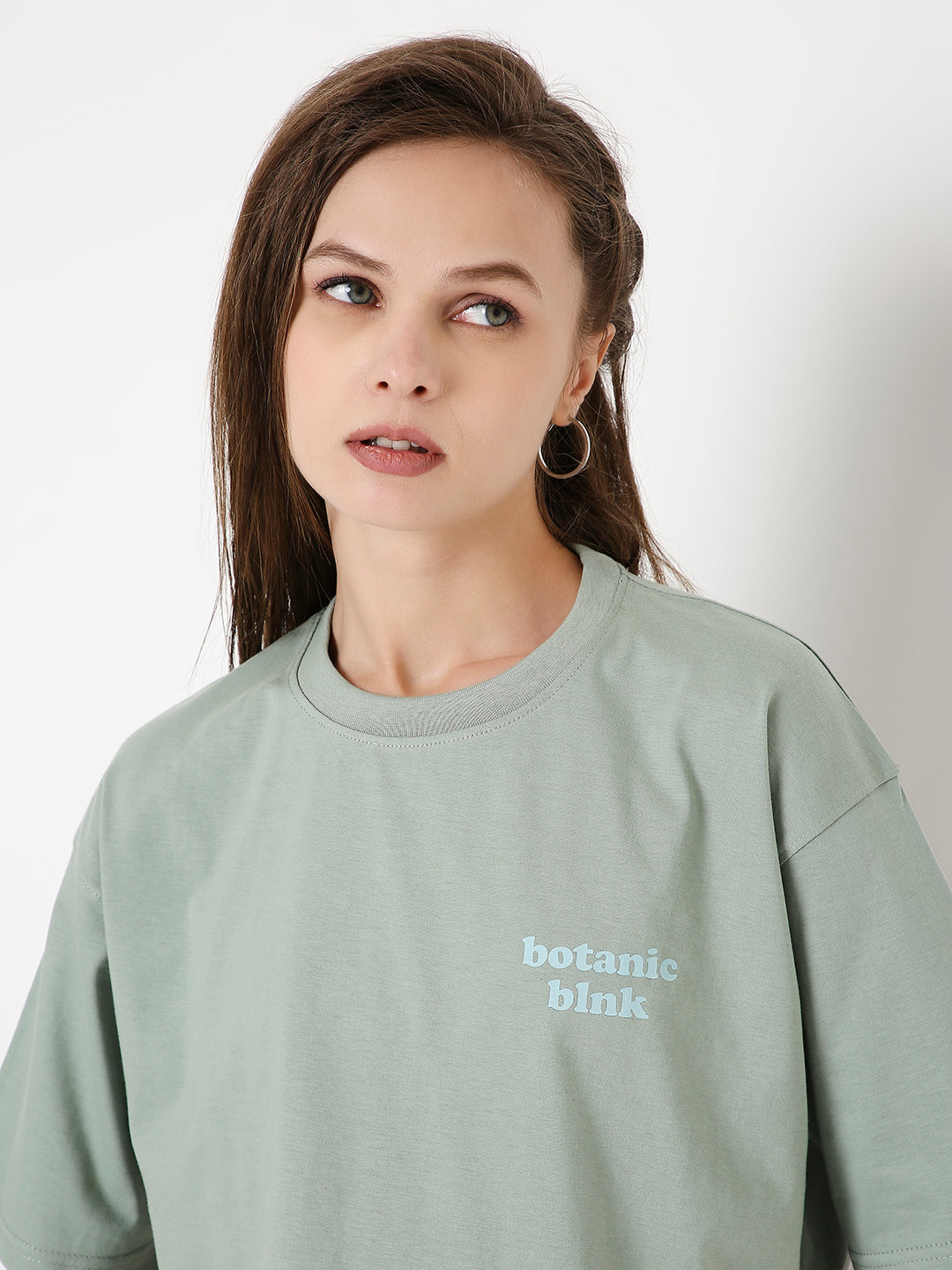 Oversize sage green crop top with small white "botanic blink" text on chest, crew neck, long sleeves.