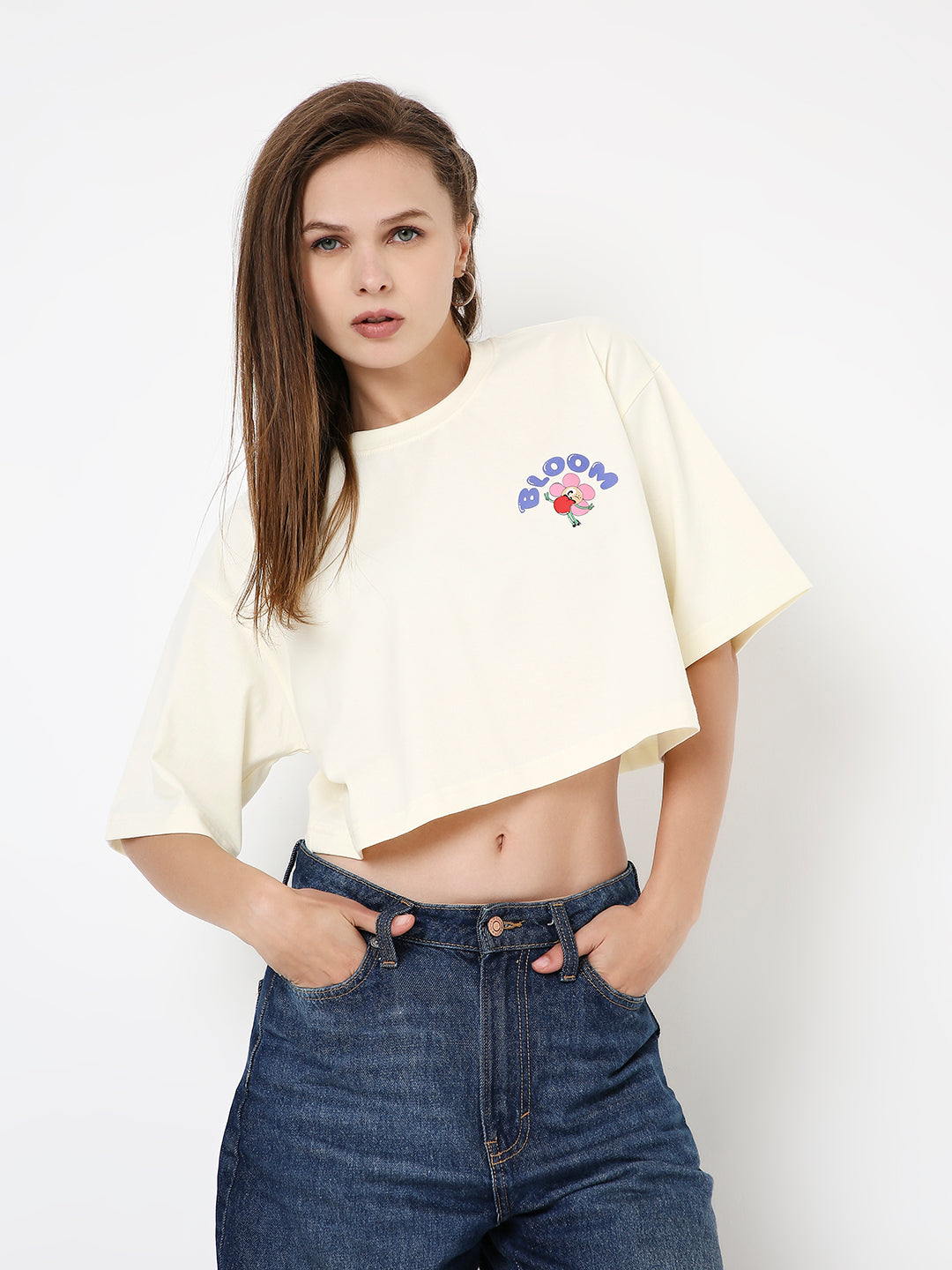 Off-white oversized cropped t-shirt with colorful flower and text print on chest, worn with high-waisted jeans.