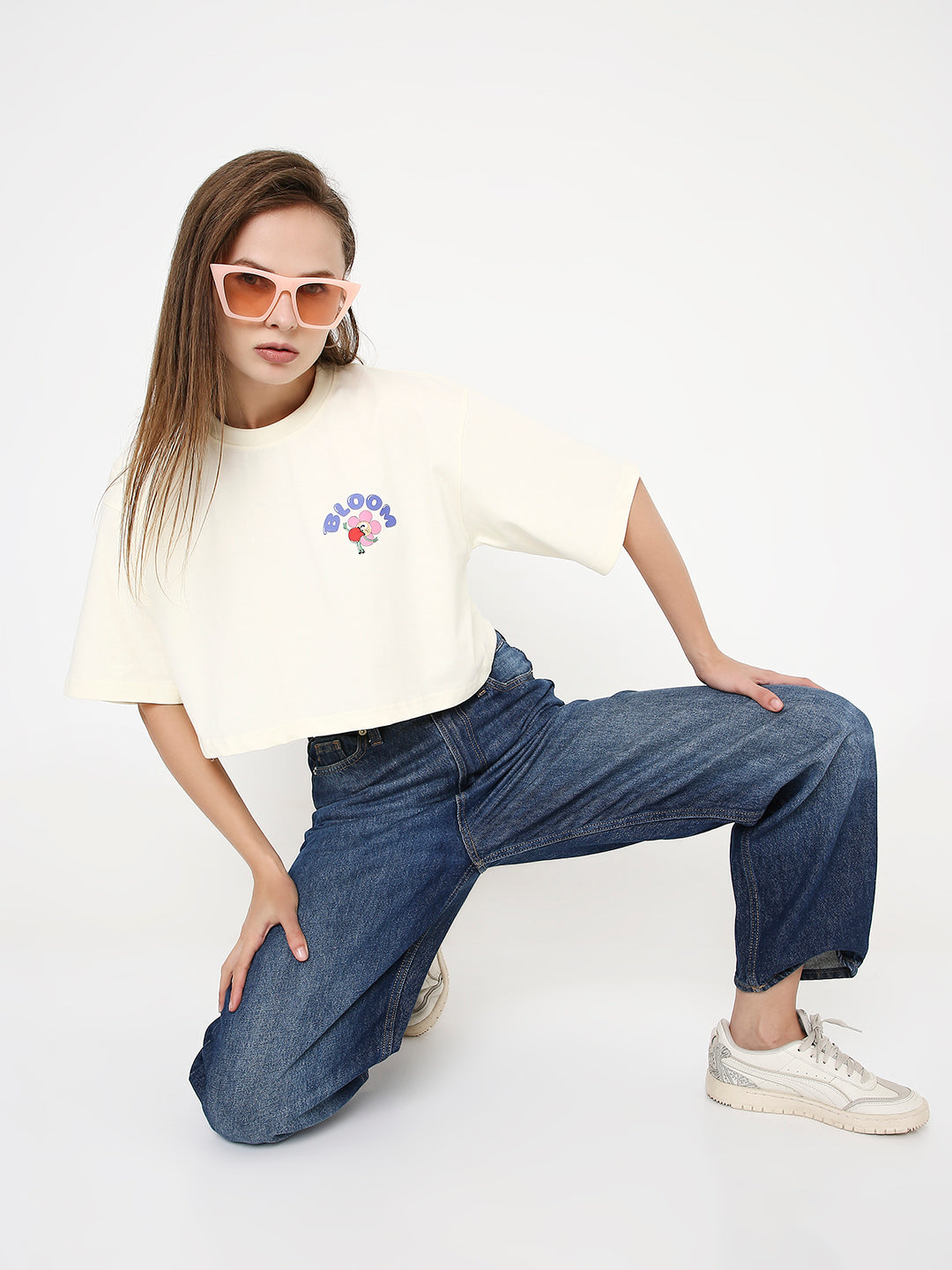 Off-white oversized cropped T-shirt with small colorful print on chest, styled with blue jeans and beige sneakers.