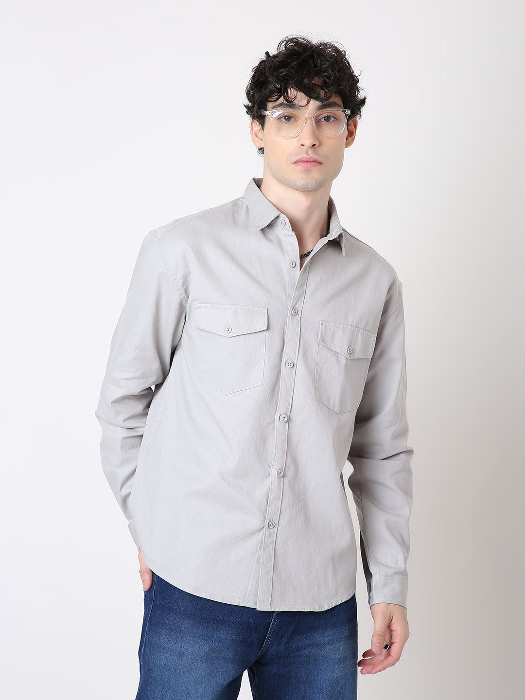 Man wearing a light gray button-up shirt and blue jeans against a white background