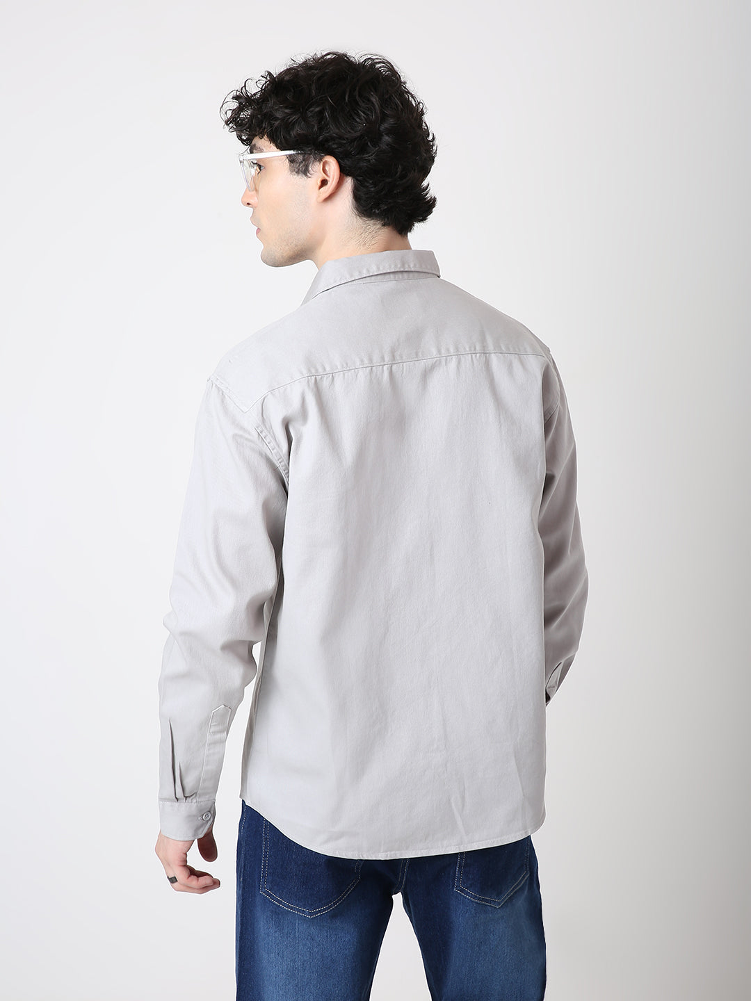 Person wearing a light gray shirt and blue jeans on a white background