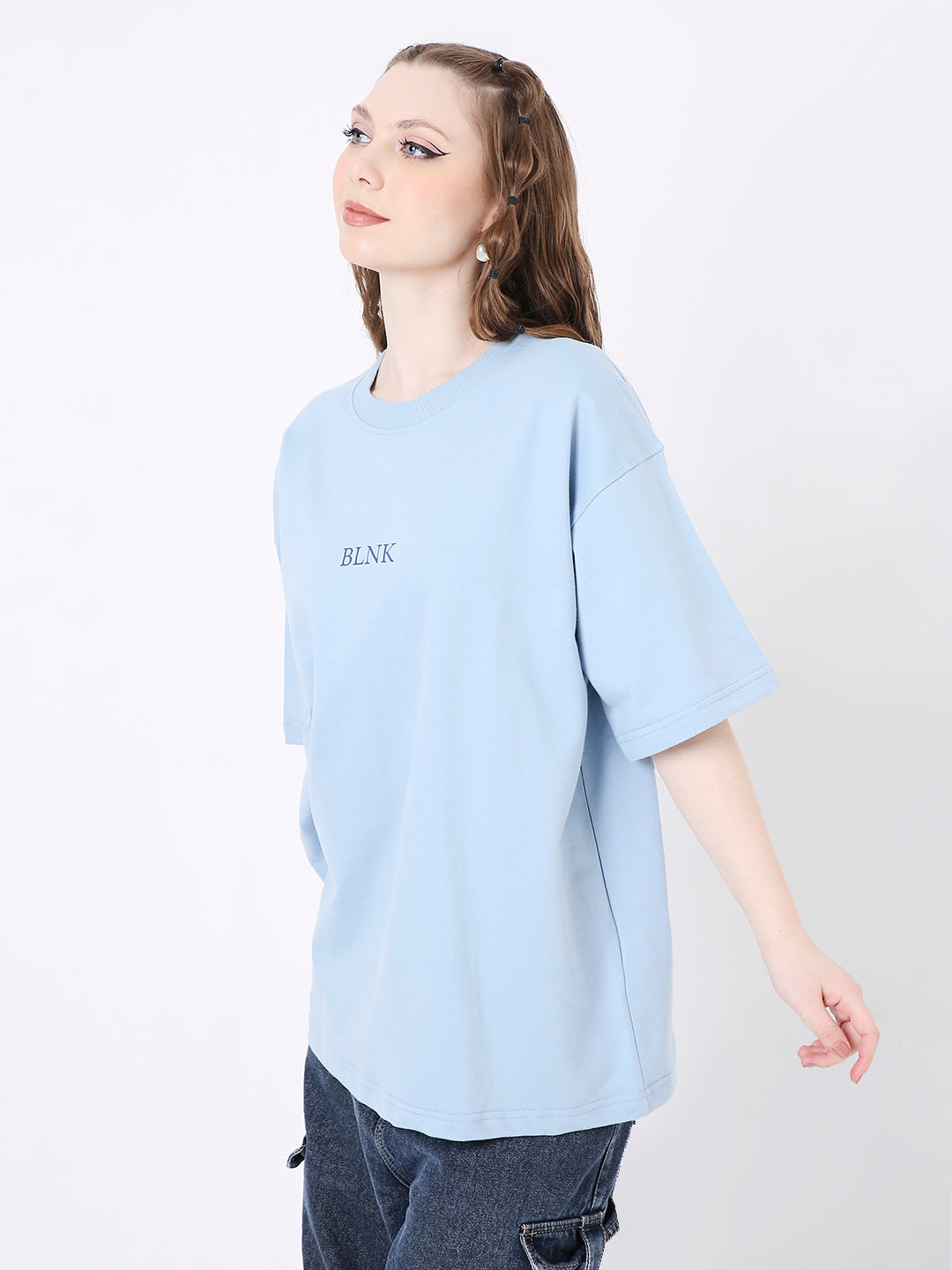 Oversize light blue T-shirt with small black printed text on chest, worn with dark jeans.