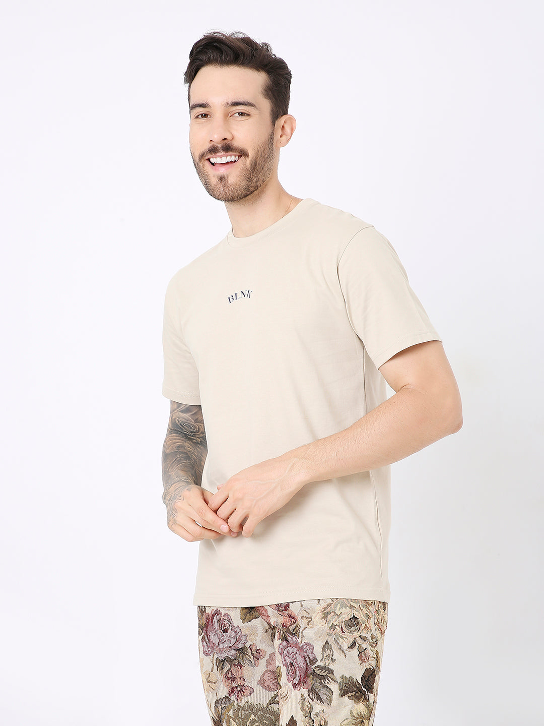 Beige relaxed fit t-shirt with small subtle printed text on chest, worn with patterned pants.